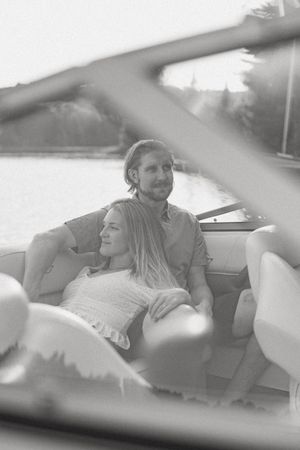 Black and white photo of a couple relaxing together on a boat near a scenic waterway.