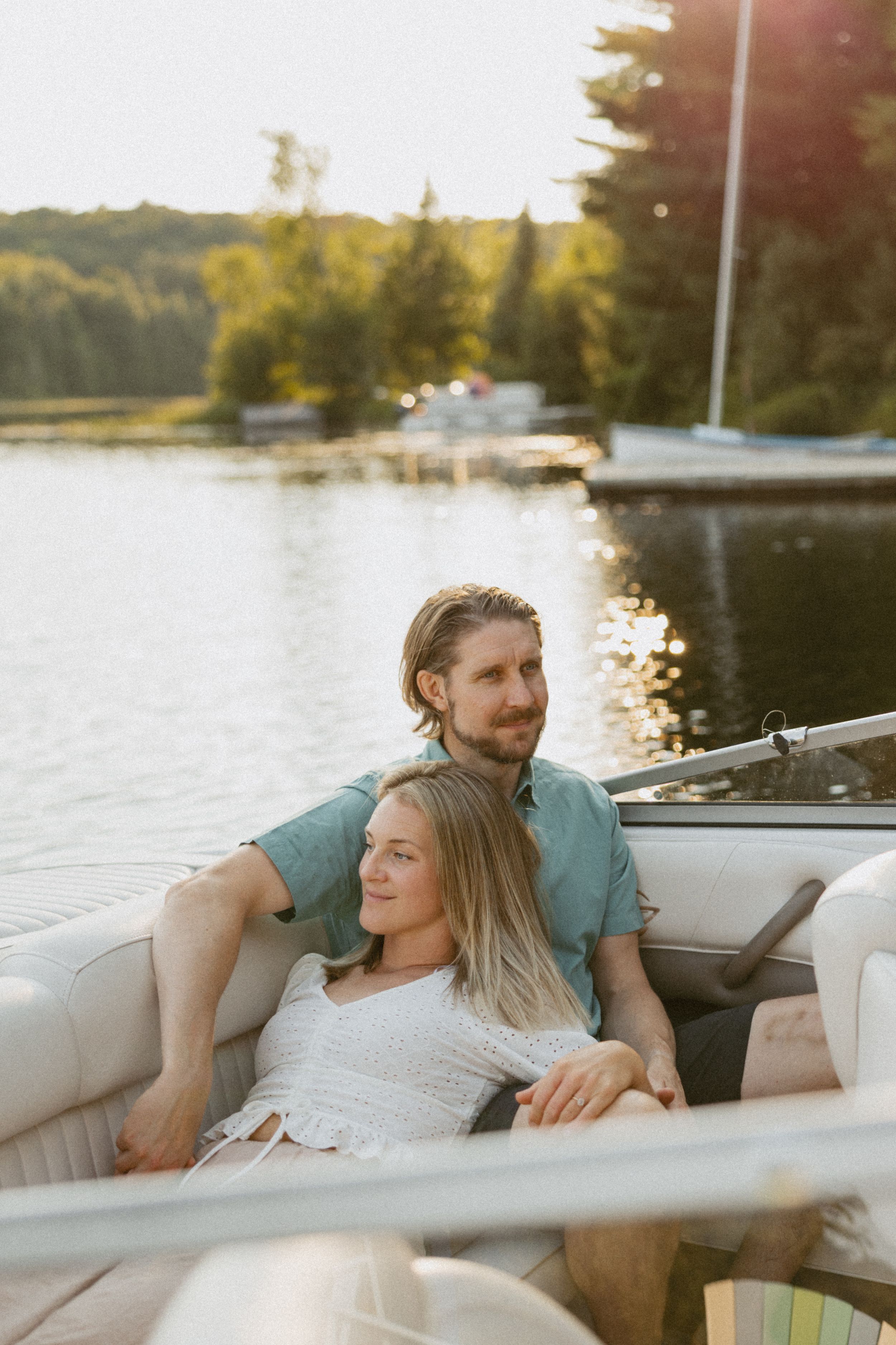 Couple relaxing together on a boat at sunset on a calm lake, surrounded by lush green trees and golden light.