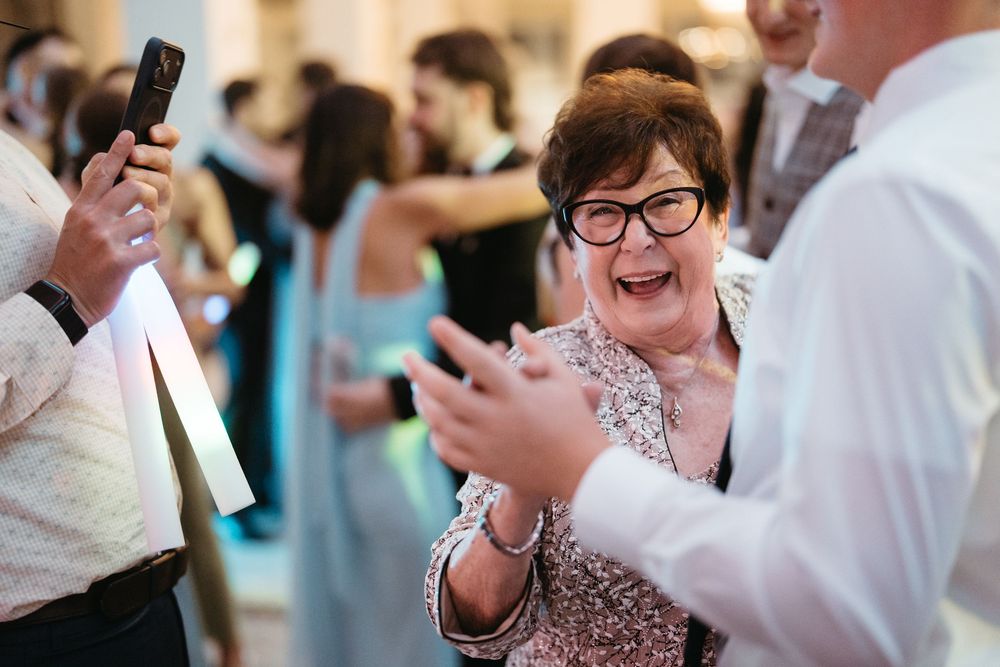 Joyful woman in sequin dress laughing and clapping at a wedding reception dance floor.