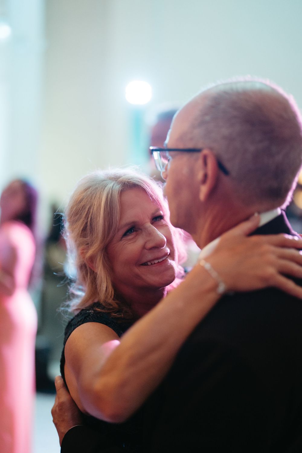 Smiling older woman dancing with a man at a formal event, wearing a black dress and bracelet.