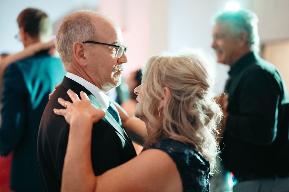 Elderly couple dancing closely together at a formal event, with other guests visible in the background.
