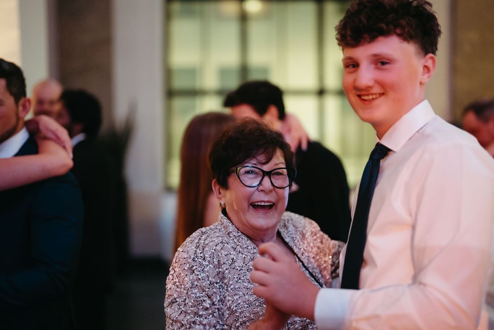 An elderly woman and young man share a joyful moment at a formal event, both smiling warmly at a celebration.