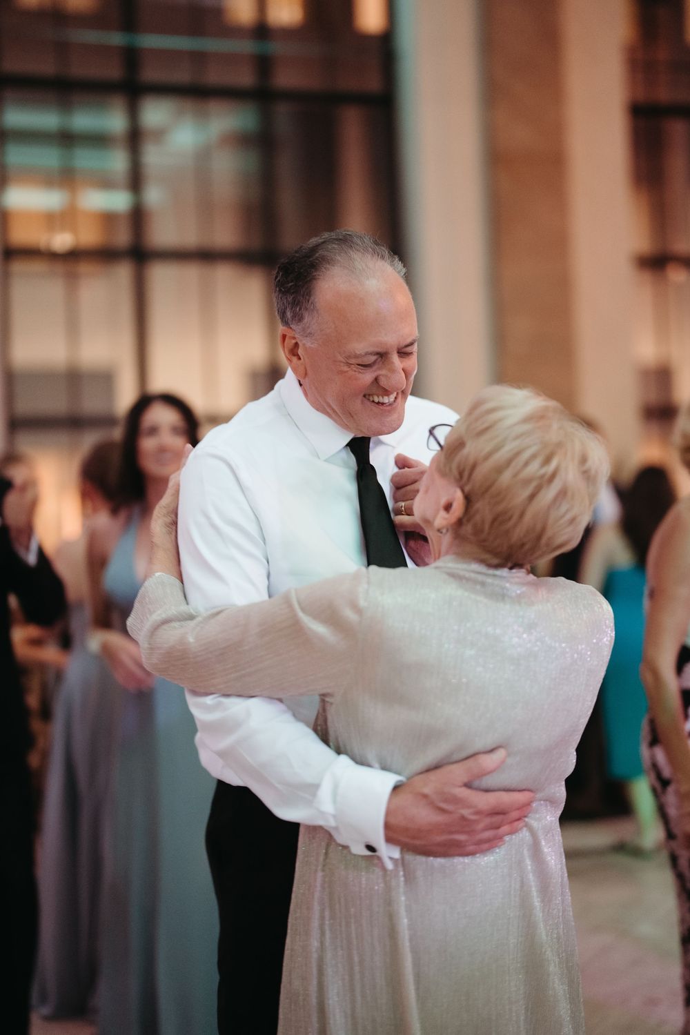 Elderly couple sharing a joyful dance embrace at a wedding reception, smiling warmly in formal attire.