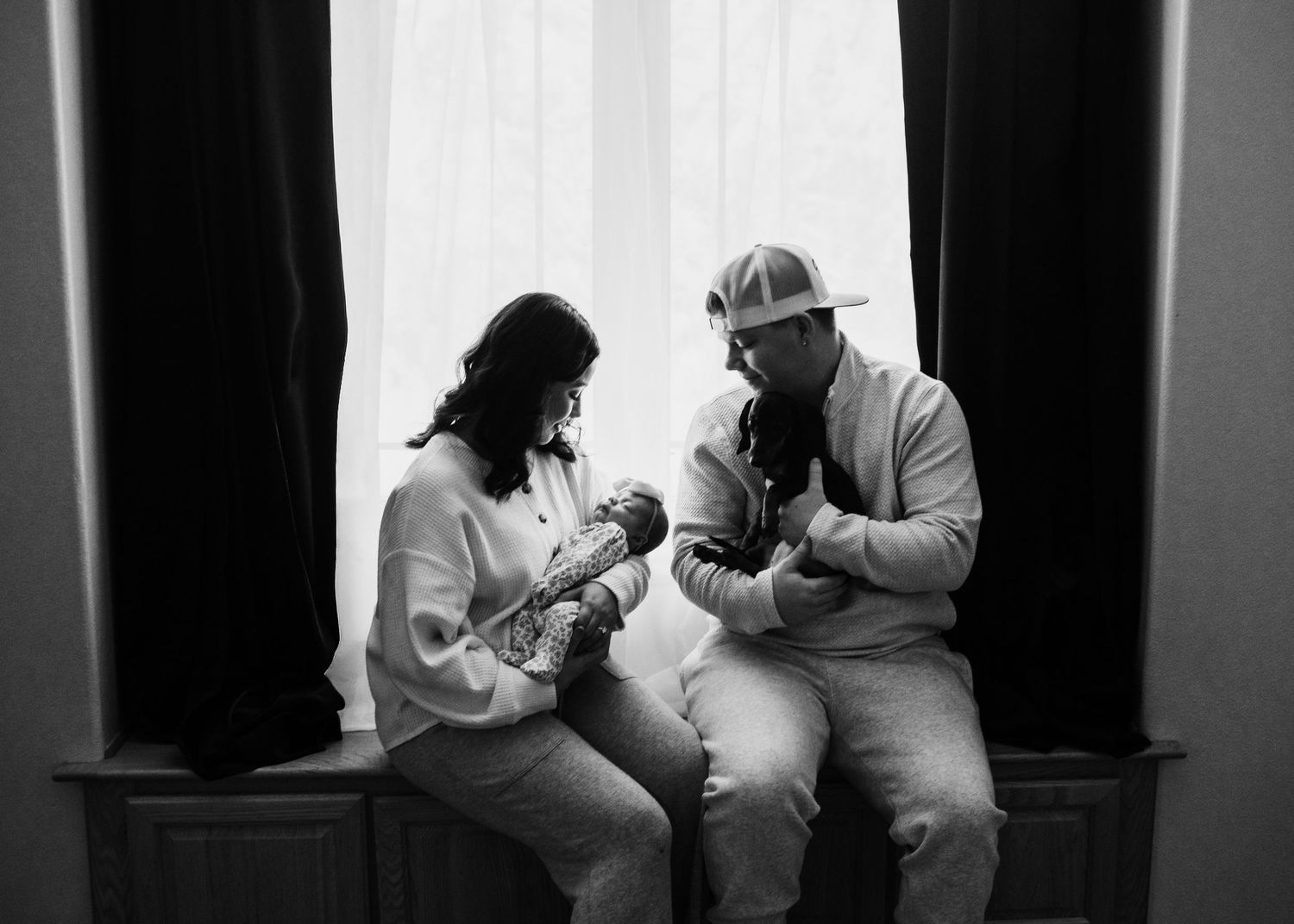Parents sitting together and holding their newborn baby at home during an in-home newborn session