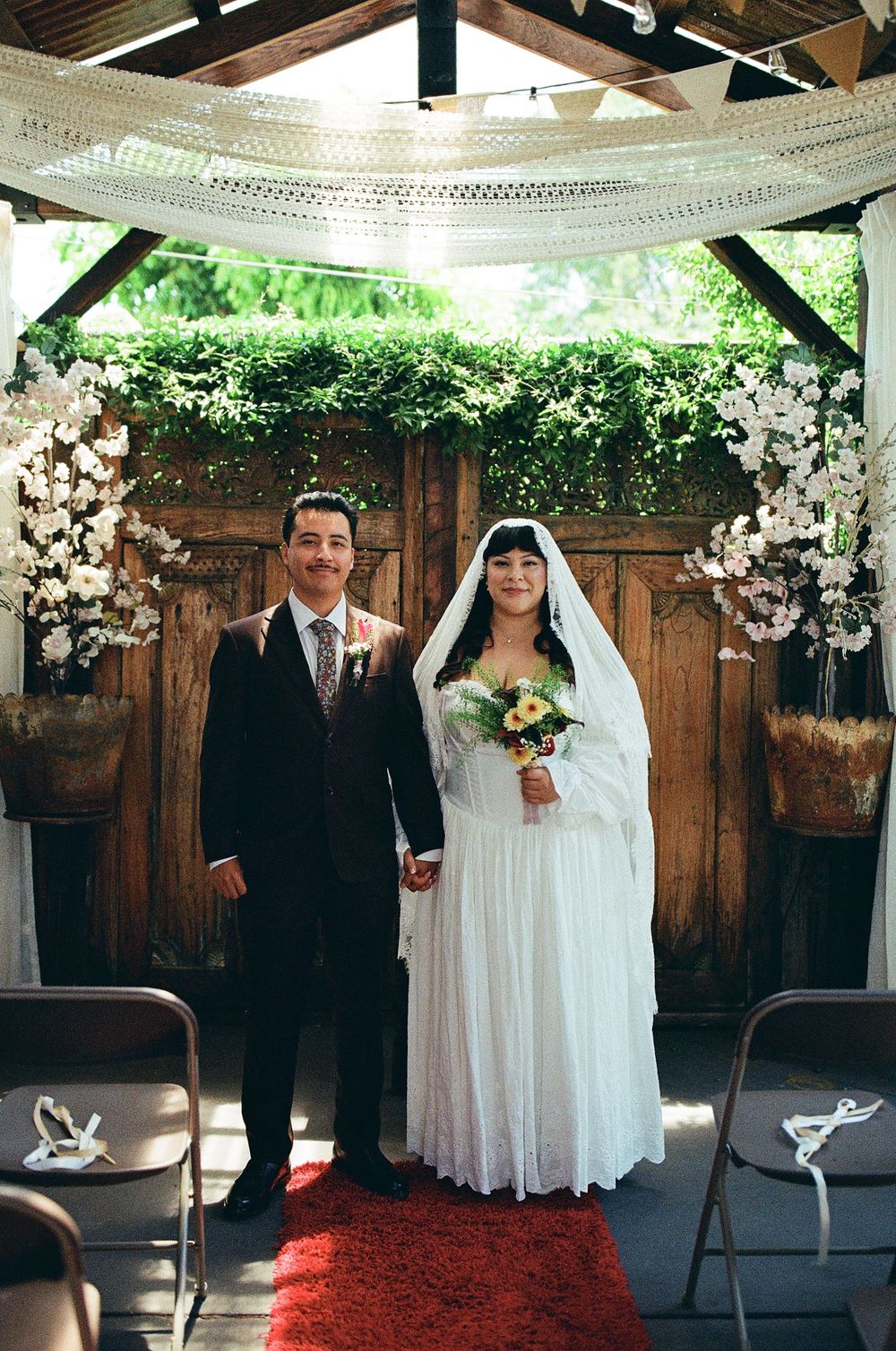 couple standing at wedding altar of old brown house smiling for camera, film wedding photography