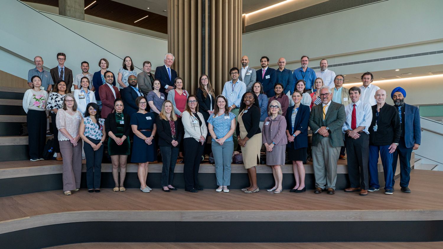 Large group of professionals posing on stairs in modern building atrium for formal group photo.