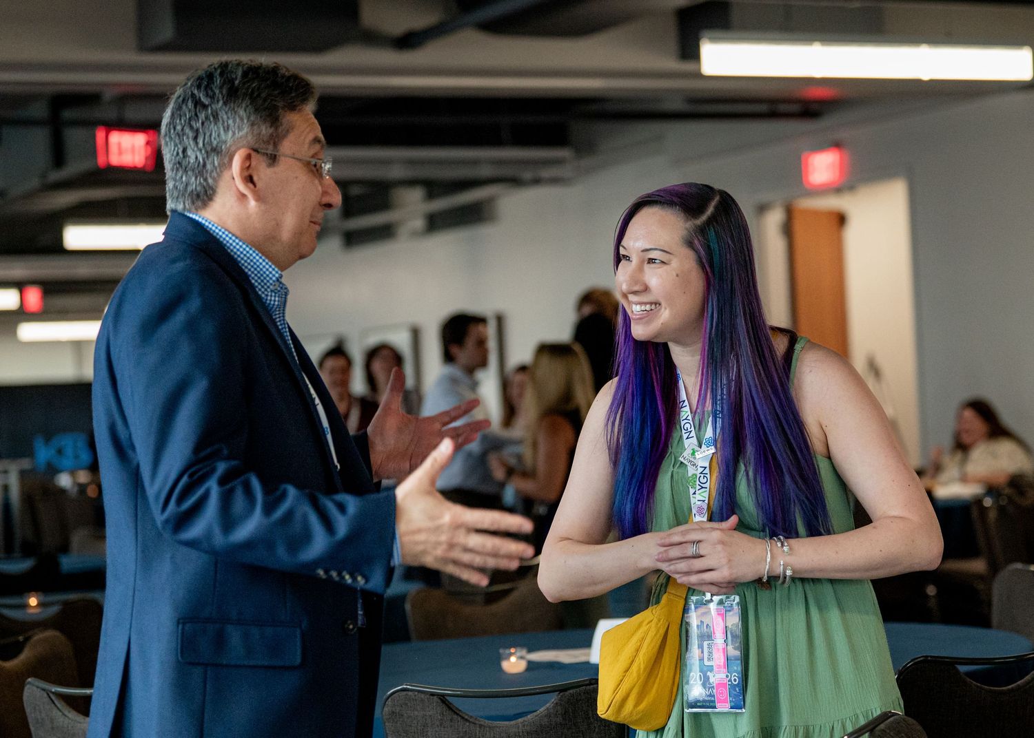 Man in blue suit shaking hands with woman with purple hair at a professional networking event.