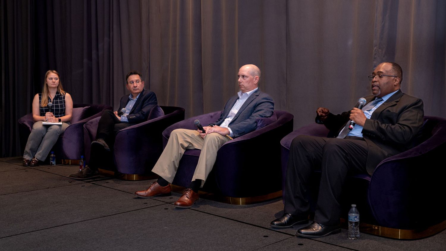 Four professionals seated on stage during a corporate panel discussion event.