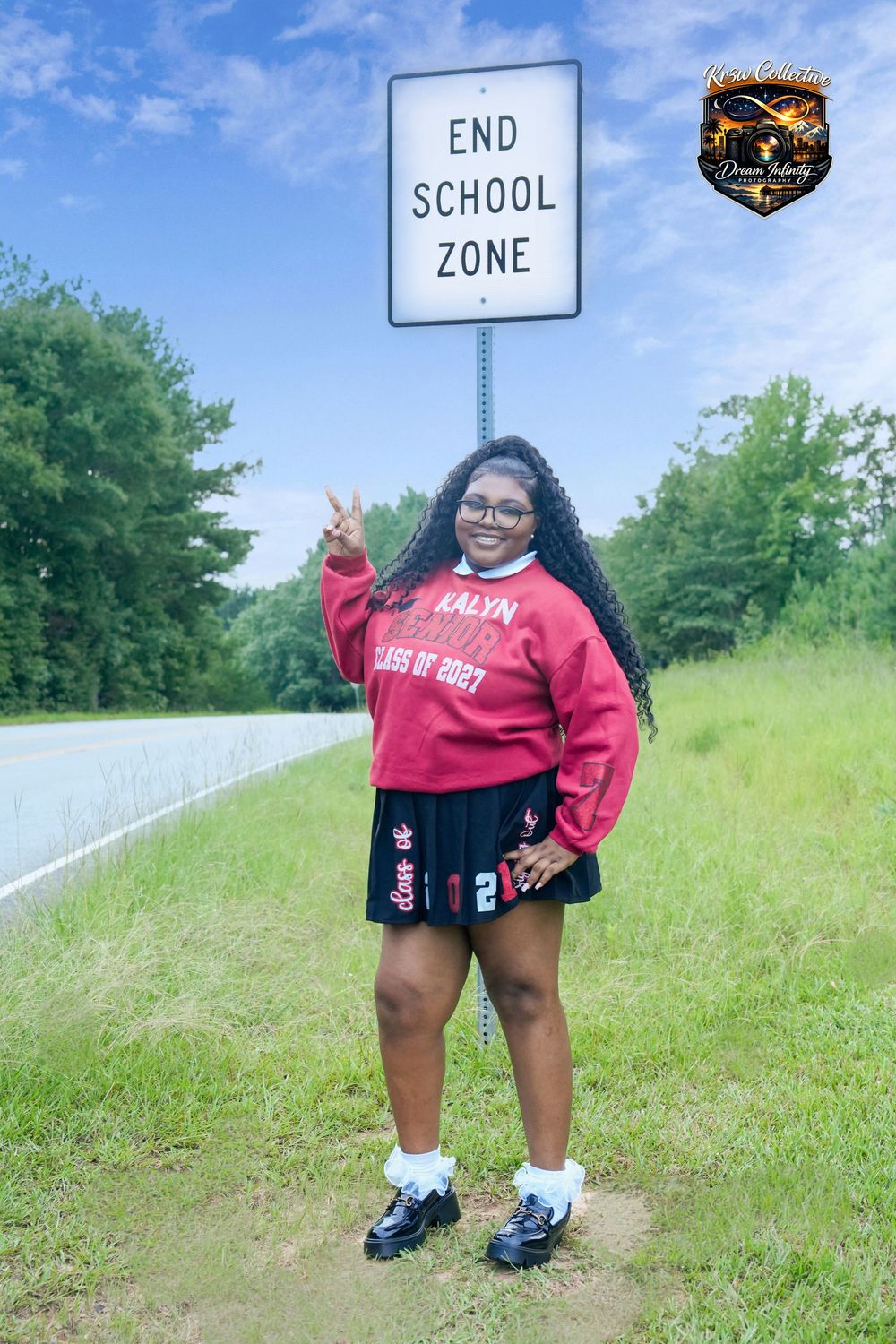 A smiling student poses in front of an End School Zone sign wearing a red Class of 2027 sweatshirt and black skirt.
