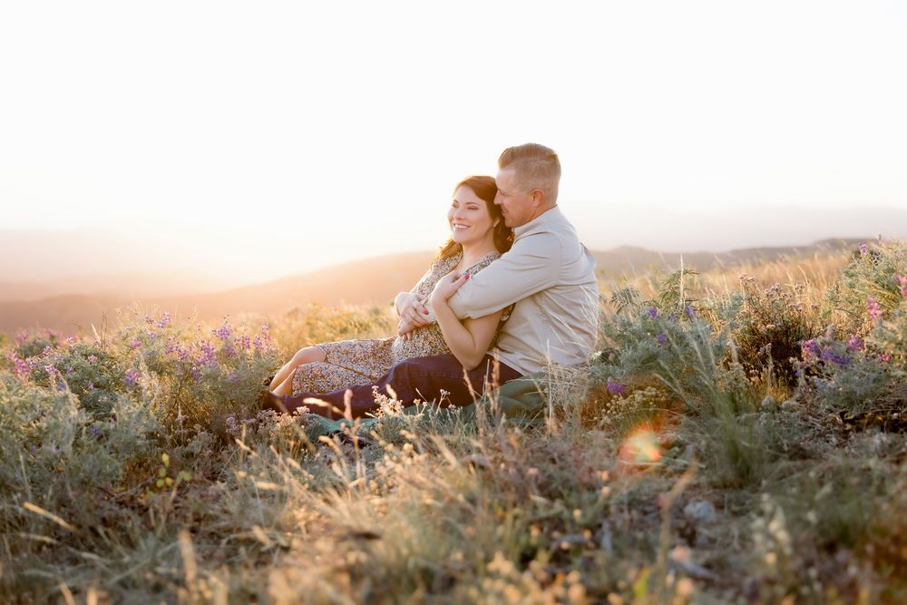 Two people share an intimate moment while sitting in a wildflower field at golden hour.