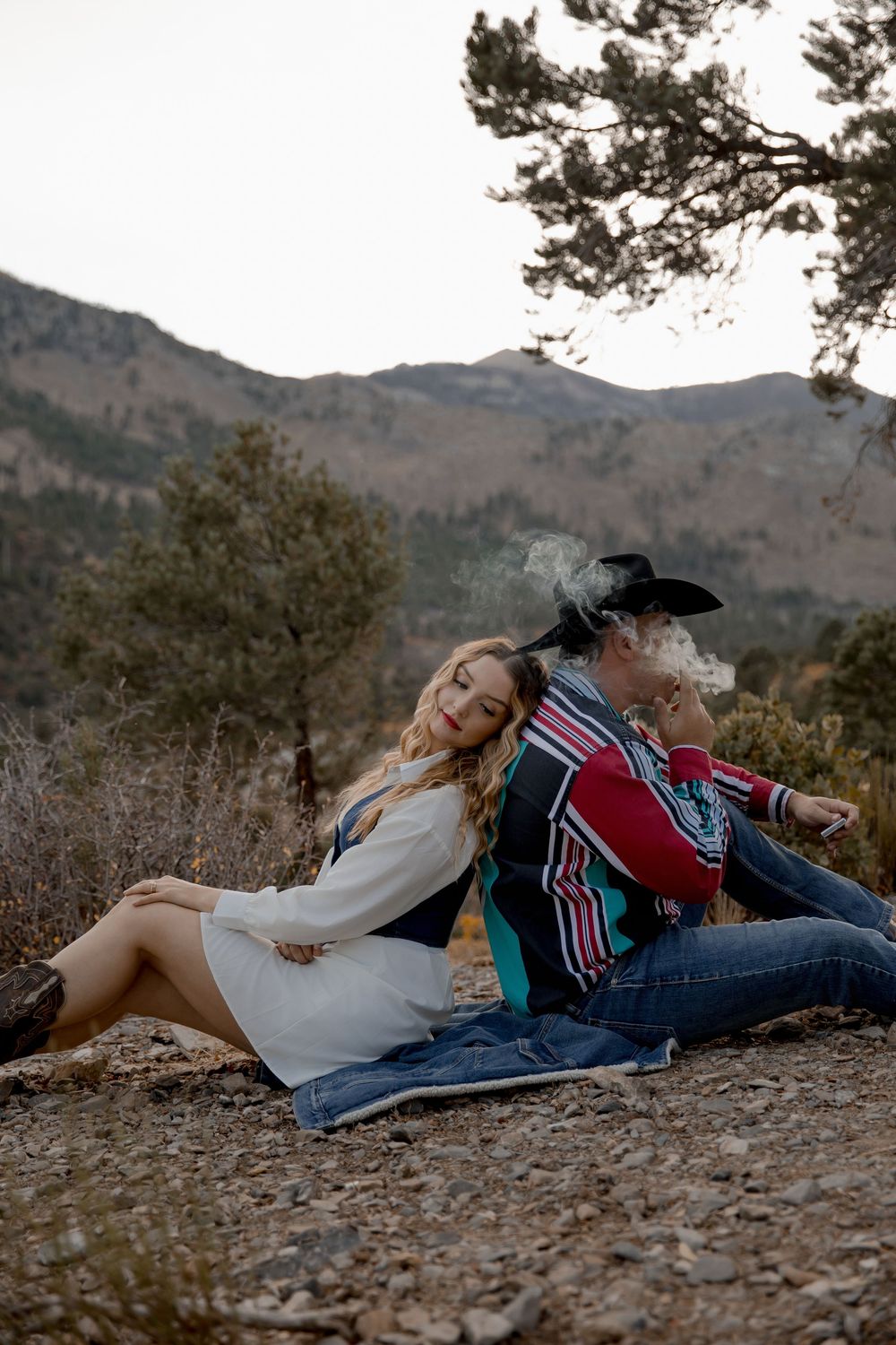 Two people relax together on a blanket against a scenic mountain backdrop during sunset.