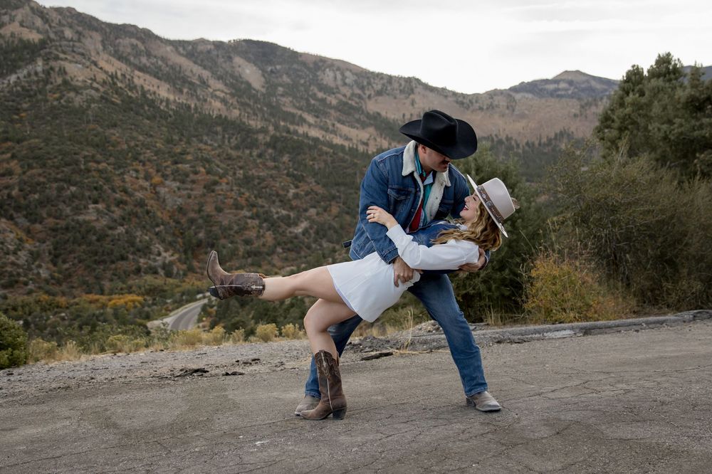A romantic couple shares a dance dip pose against a scenic mountain landscape backdrop during sunset.