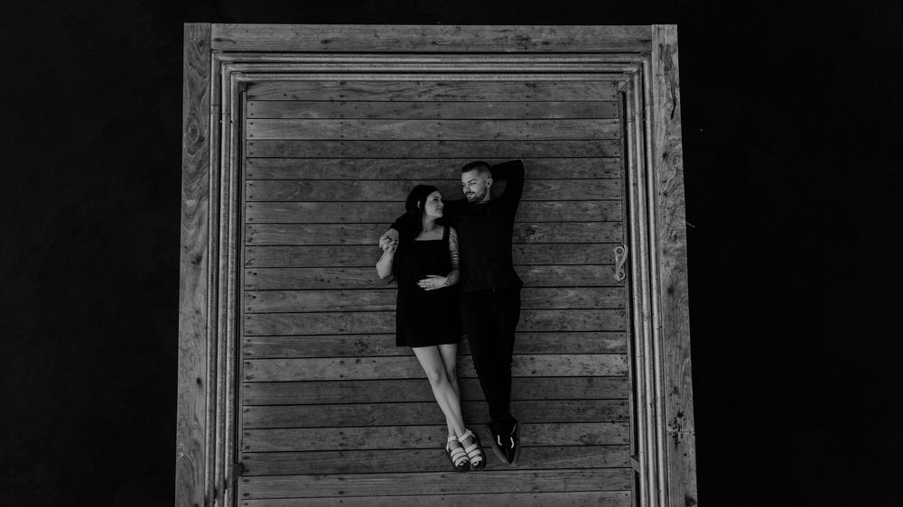 Black and white overhead view of a person lying on a wooden surface in a dark dress.