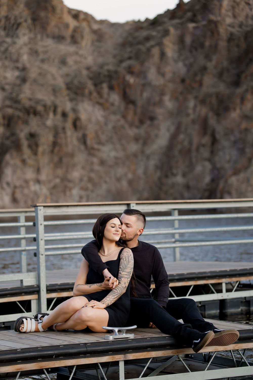 Romantic couple sharing intimate moments while sitting on bleachers against rocky cliffs at sunset.