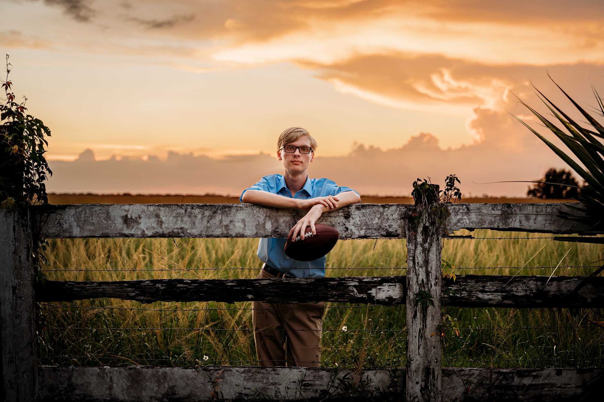 senior boy posing on a fence during sunset with a football