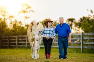 man and woman walking with a paint horse during golden hour