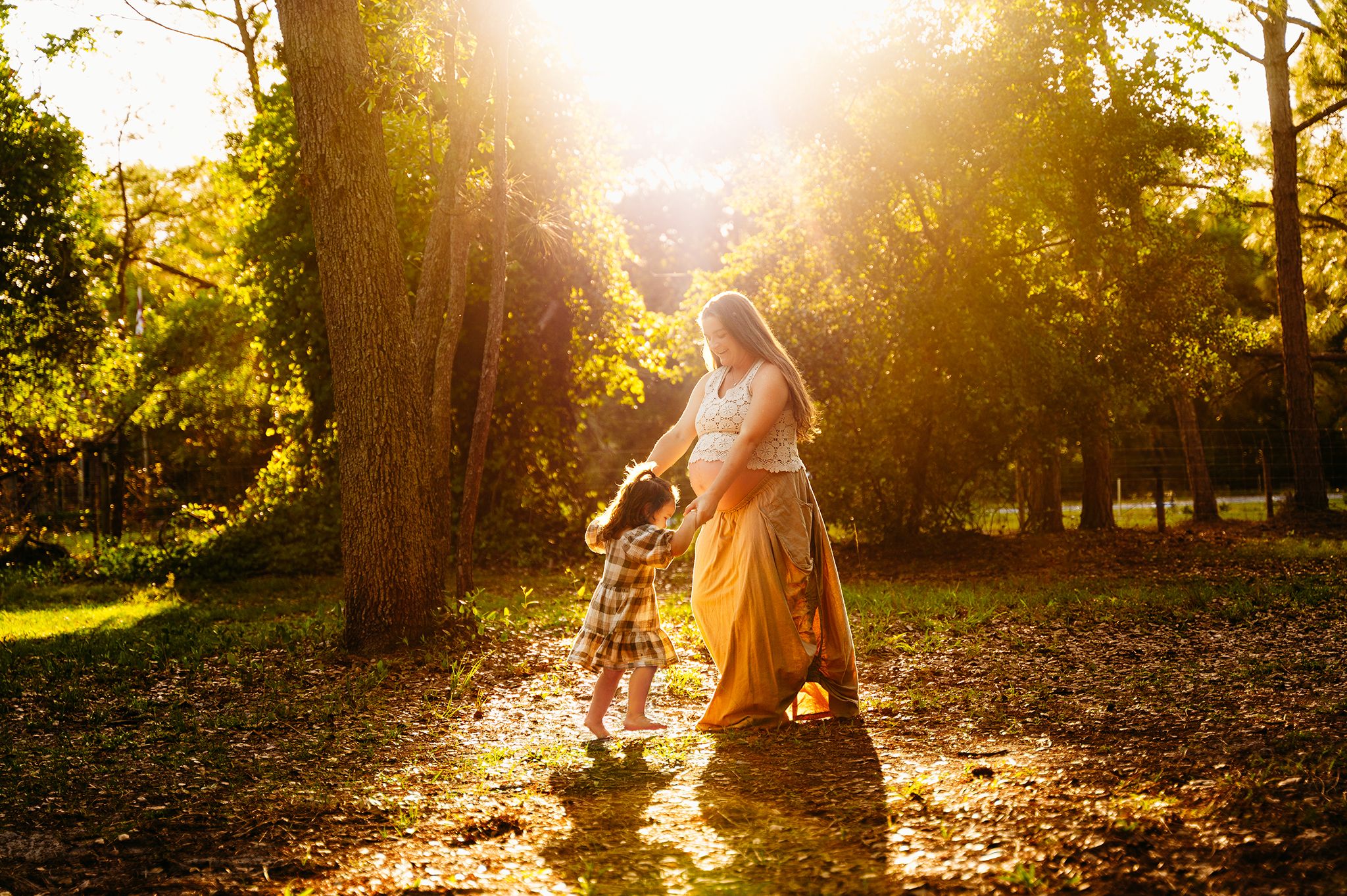homestead style maternity session with pregnant mom in a yellow skirt dancing in a circle with her toddler
