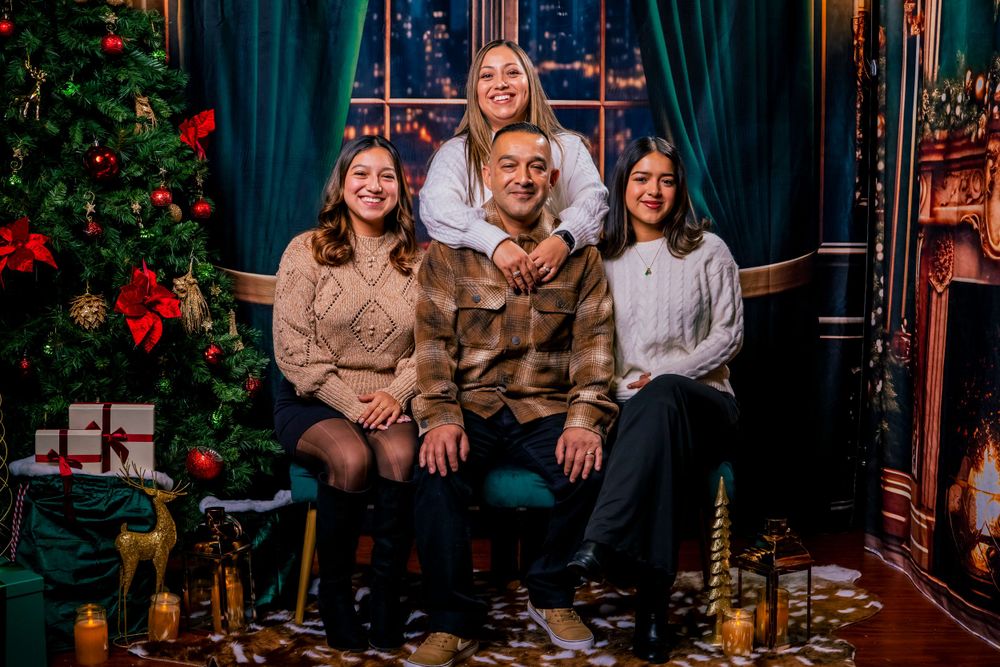 Family Christmas photo with decorated tree and wrapped presents in cozy indoor setting.