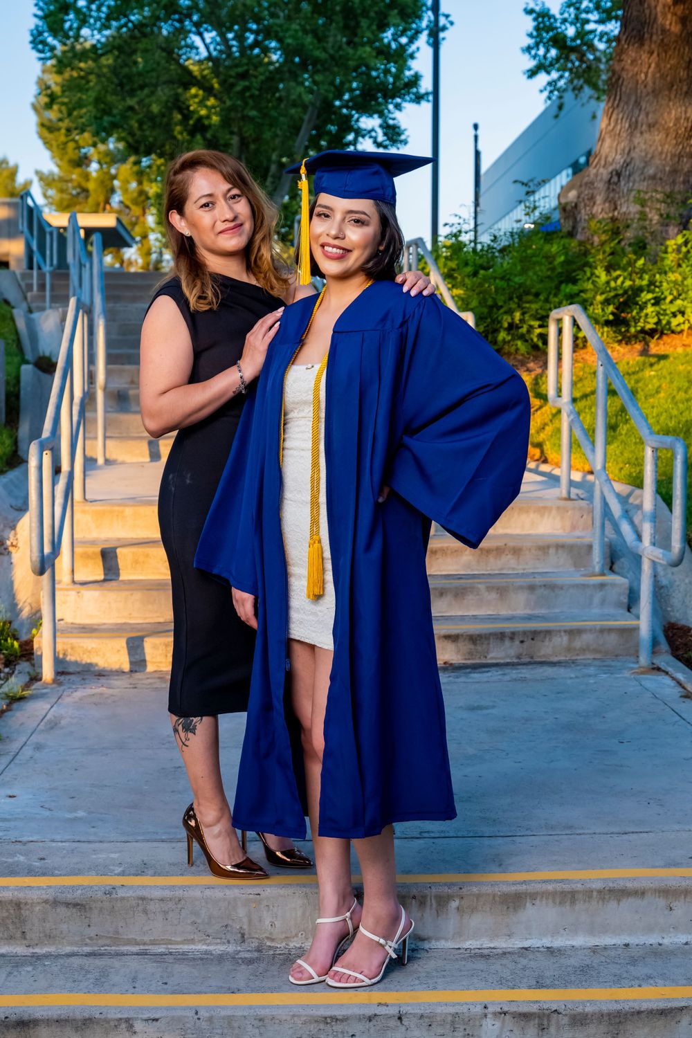 Two people pose together on outdoor steps during a graduation photoshoot in evening light.