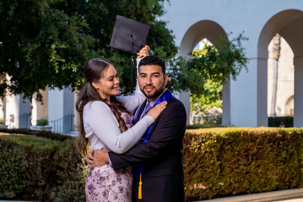 A graduation celebration photo in front of an ornate white archway and hedges.