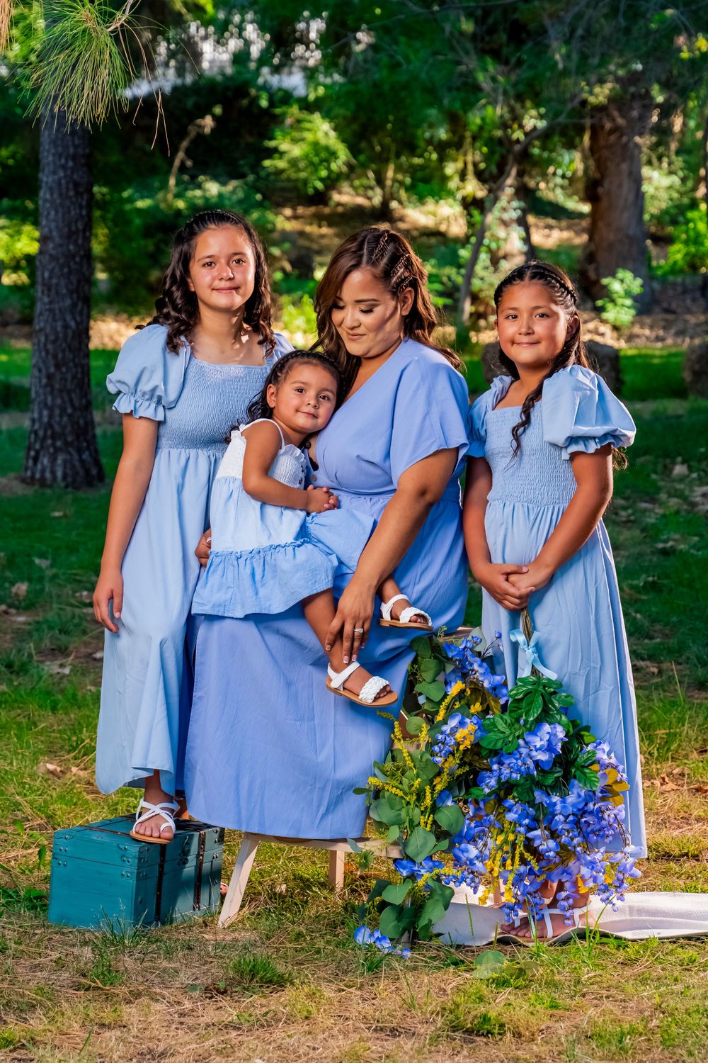 Group wearing matching blue dresses pose together outdoors with blue flowers.
