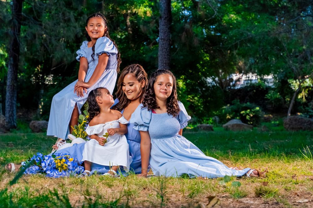 Group wearing coordinated blue dresses pose together on grass with flowers. granada hills.