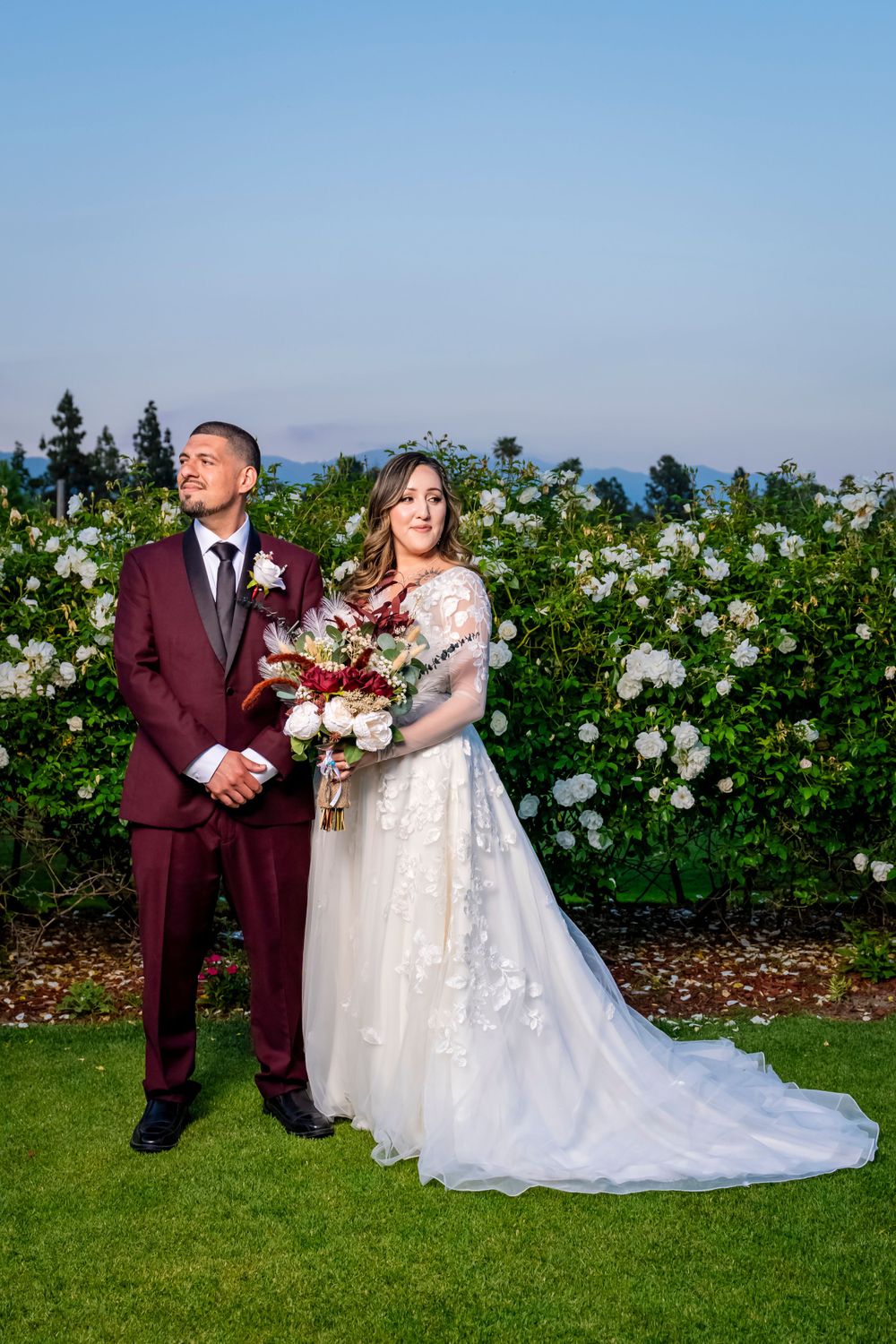 Wedding couple stands back-to-back in formal attire against garden of white roses. granada hills wedding.