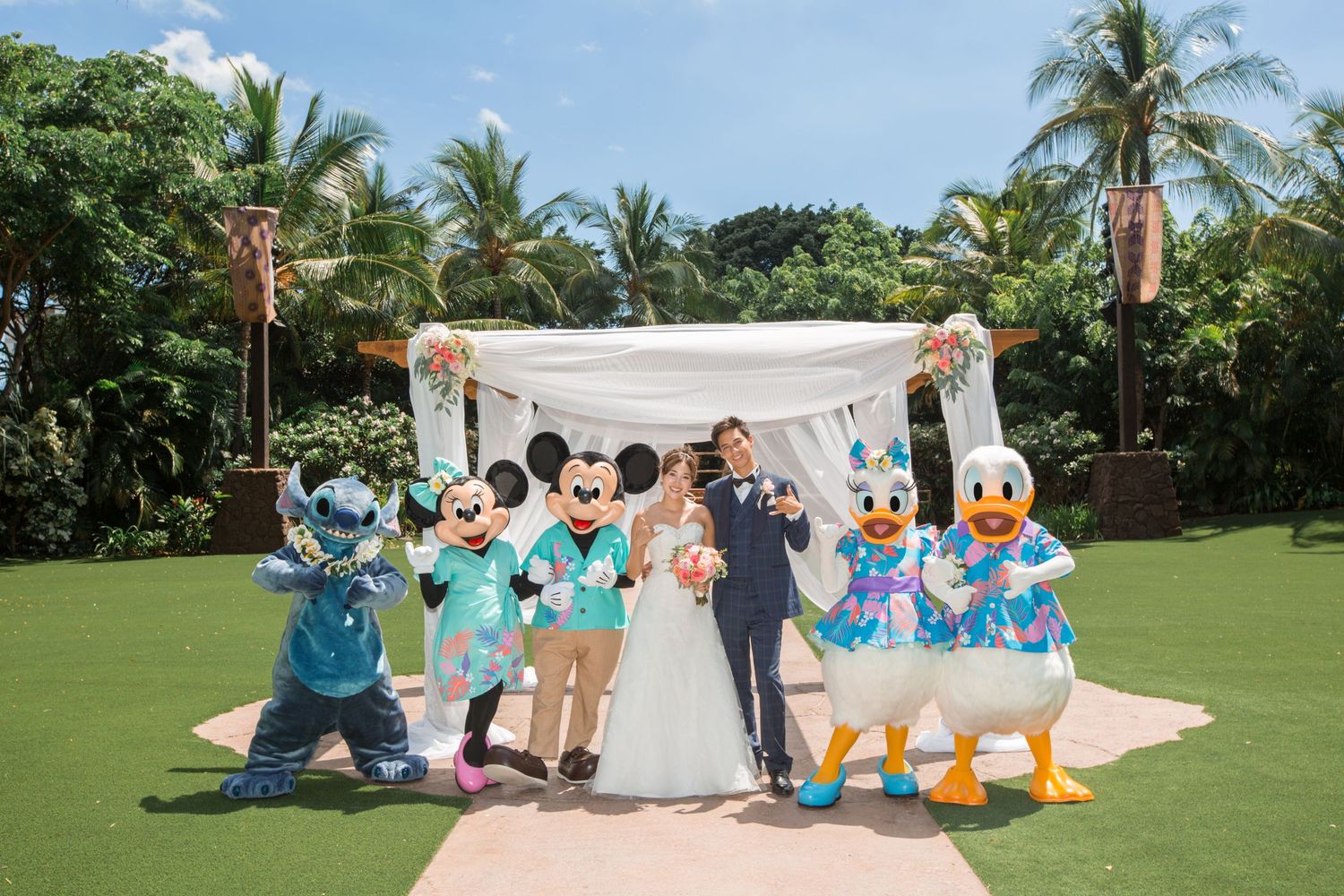 Bride and groom pose with Disney characters Mickey, Minnie, Stitch, and Donald Duck at an outdoor wedding ceremony.
アウラニディズニーフェアリーテールウェディング