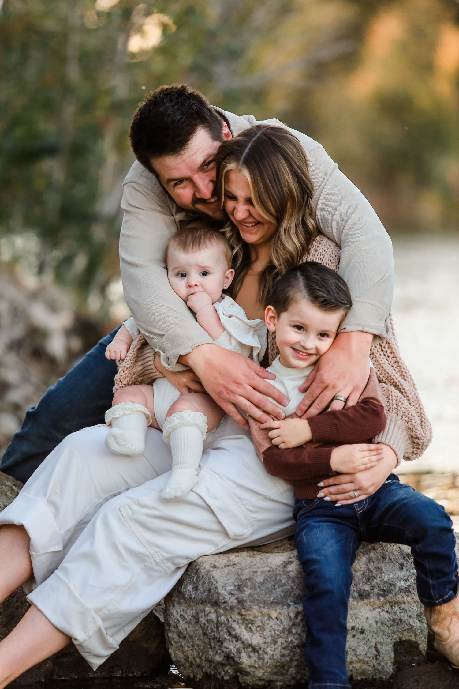 Family cuddles together on rocks during outdoor photo session.