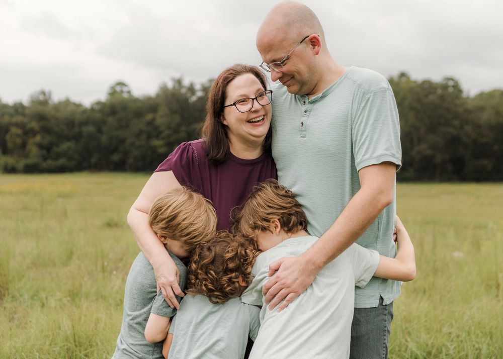 A loving family shares an intimate moment together while standing in a sunlit meadow on a warm afternoon.