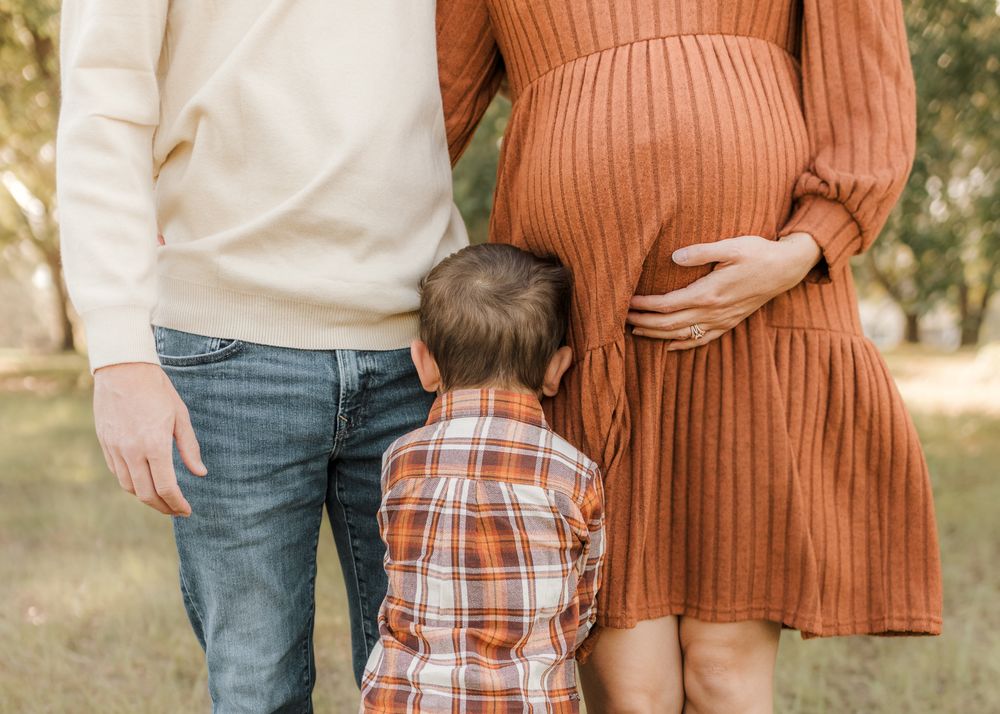 Family wearing coordinated fall outfits in orange and plaid standing together in a park setting.