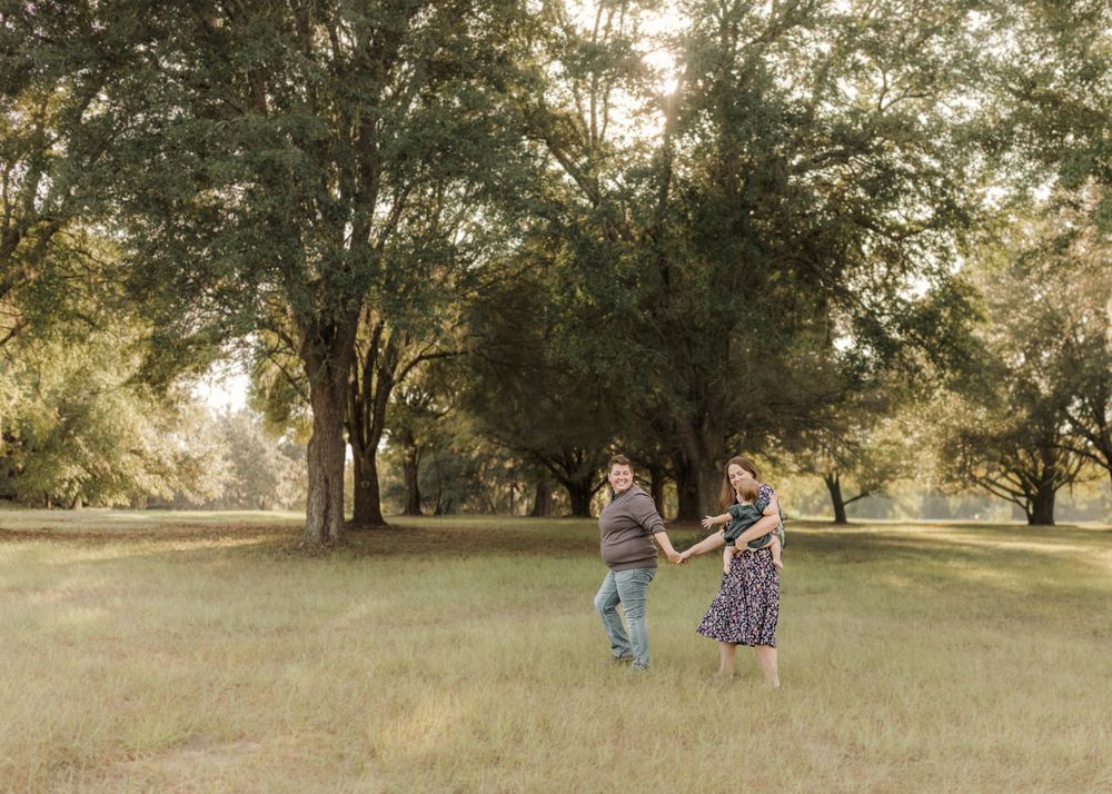 A family walks together through a grassy field at sunset with tall trees creating a natural backdrop.
