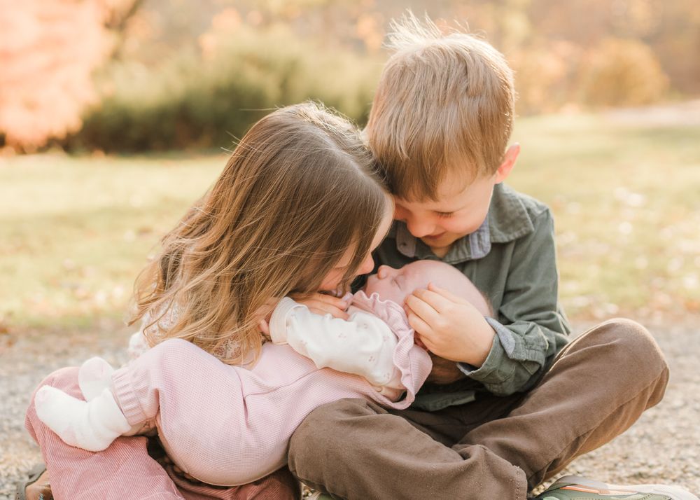 Two young children sitting close together on grass during golden hour sharing a tender moment.