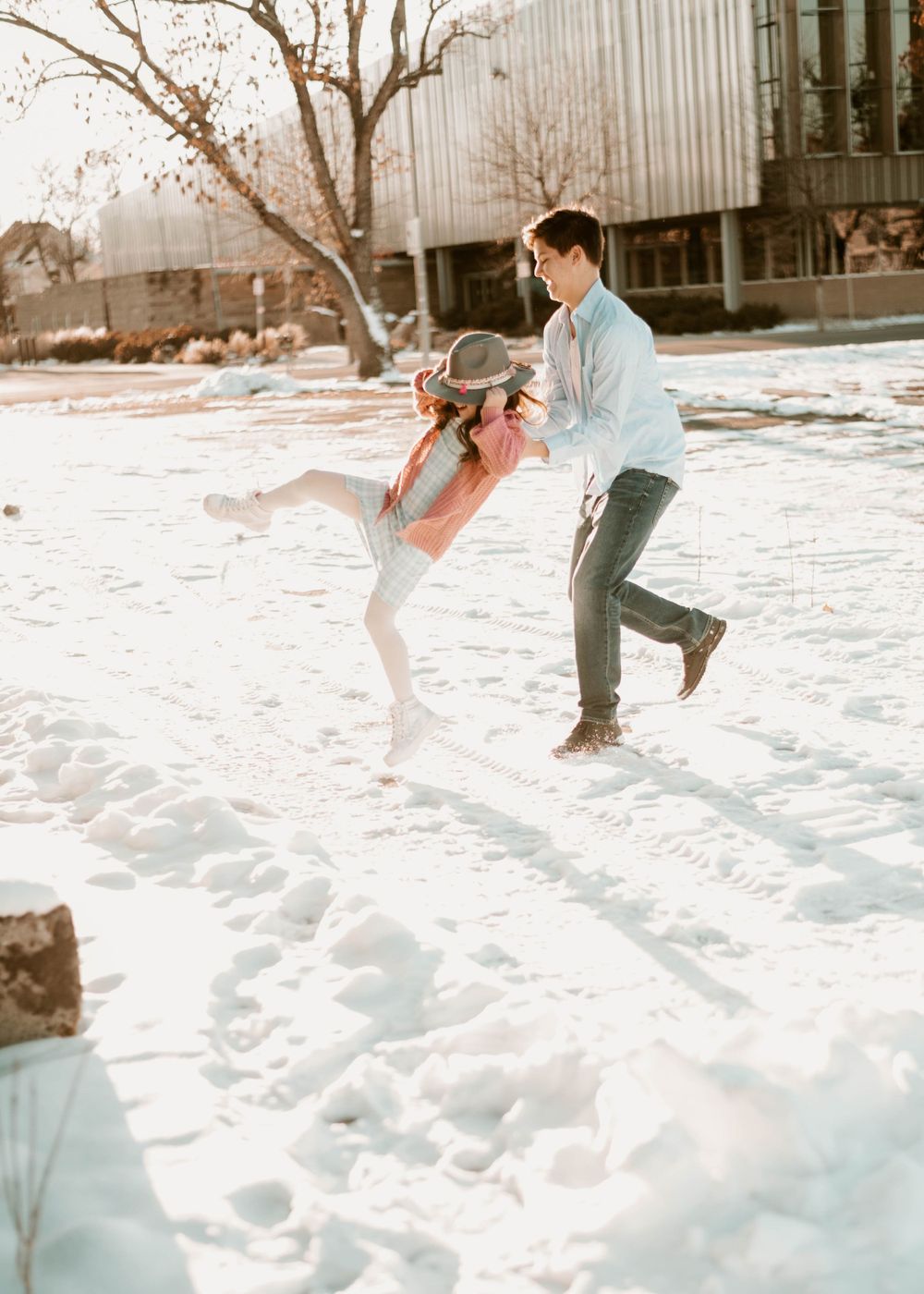 A couple plays and dances together in the snow on a sunny winter day.