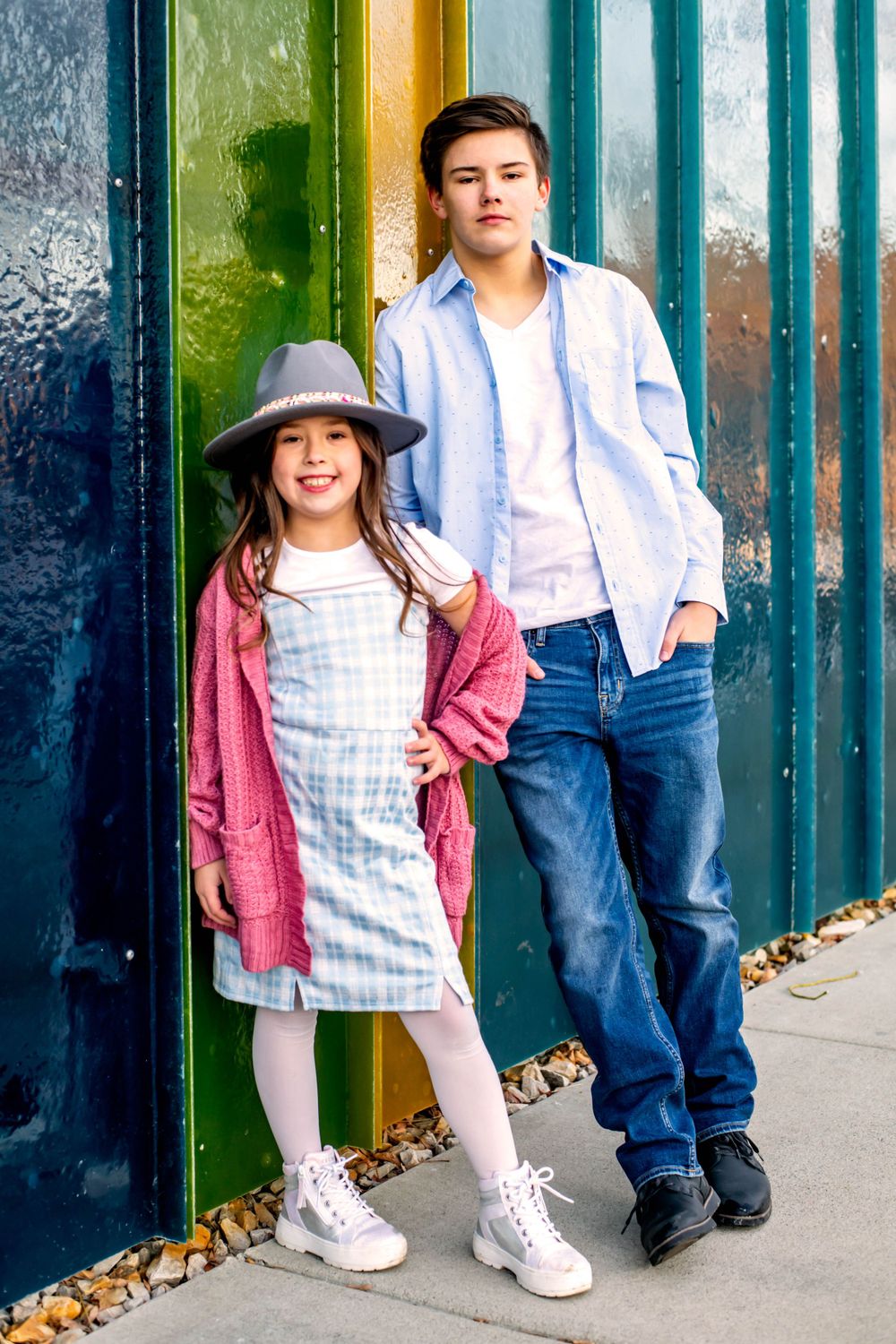 Two figures pose against a colorful striped wall in coordinated casual outfits.