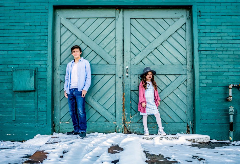 Two people pose against a vibrant turquoise door in winter with snow on the ground.