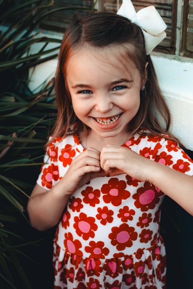 A child in a red and white floral dress shows a series of playful expressions while posing against a natural background.
