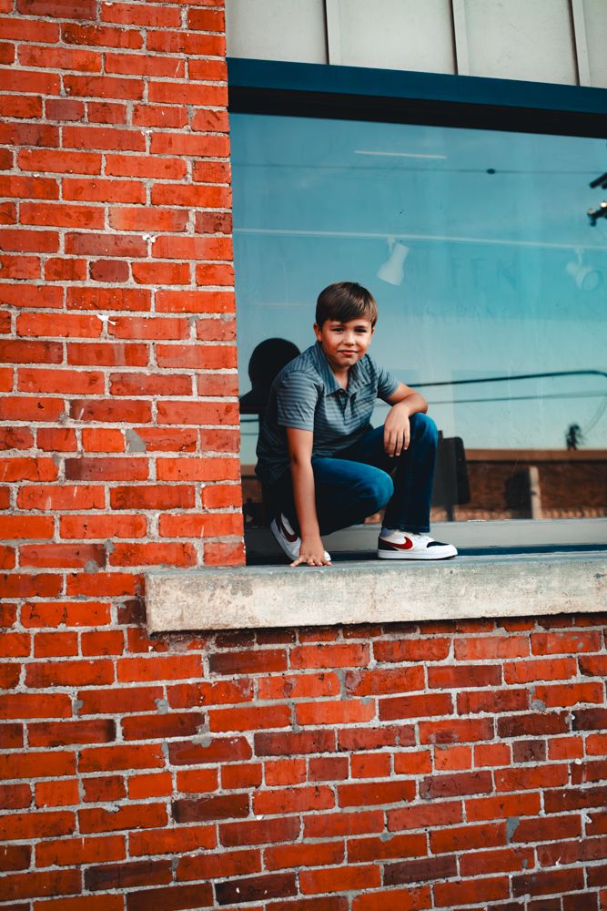 Person sitting on a window ledge against red brick wall with blue sky in background.