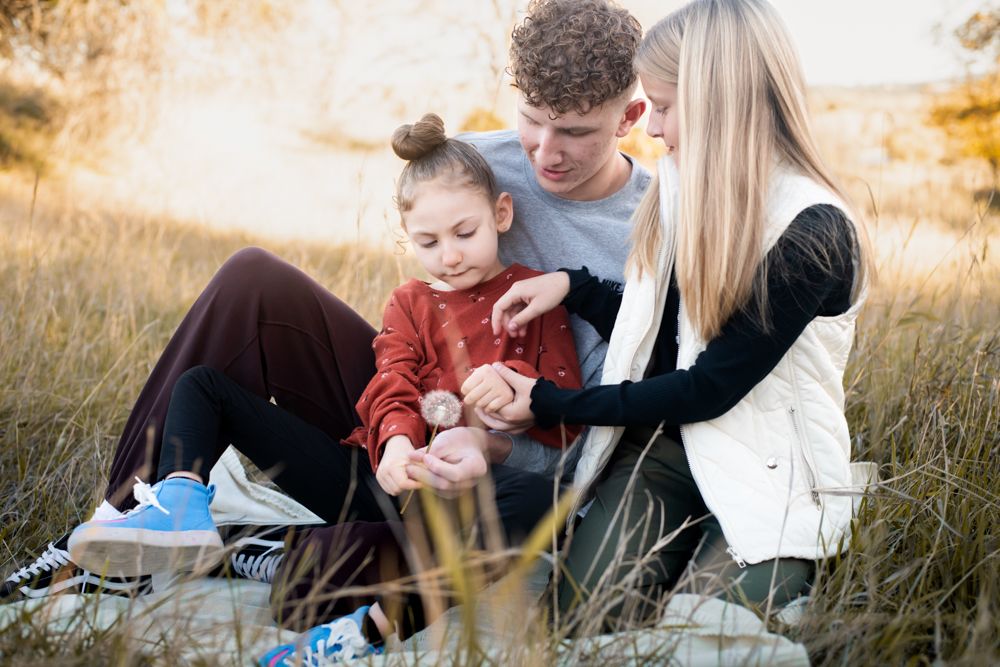 A young family sits together in a golden field during sunset.