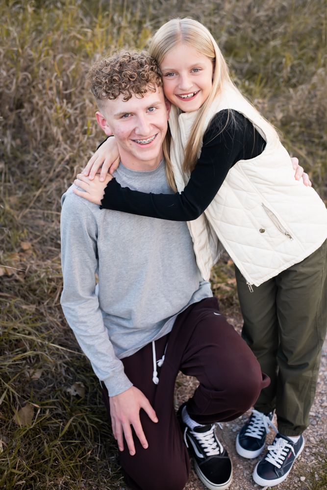 Two people share a playful embrace while posing outdoors in casual wear.