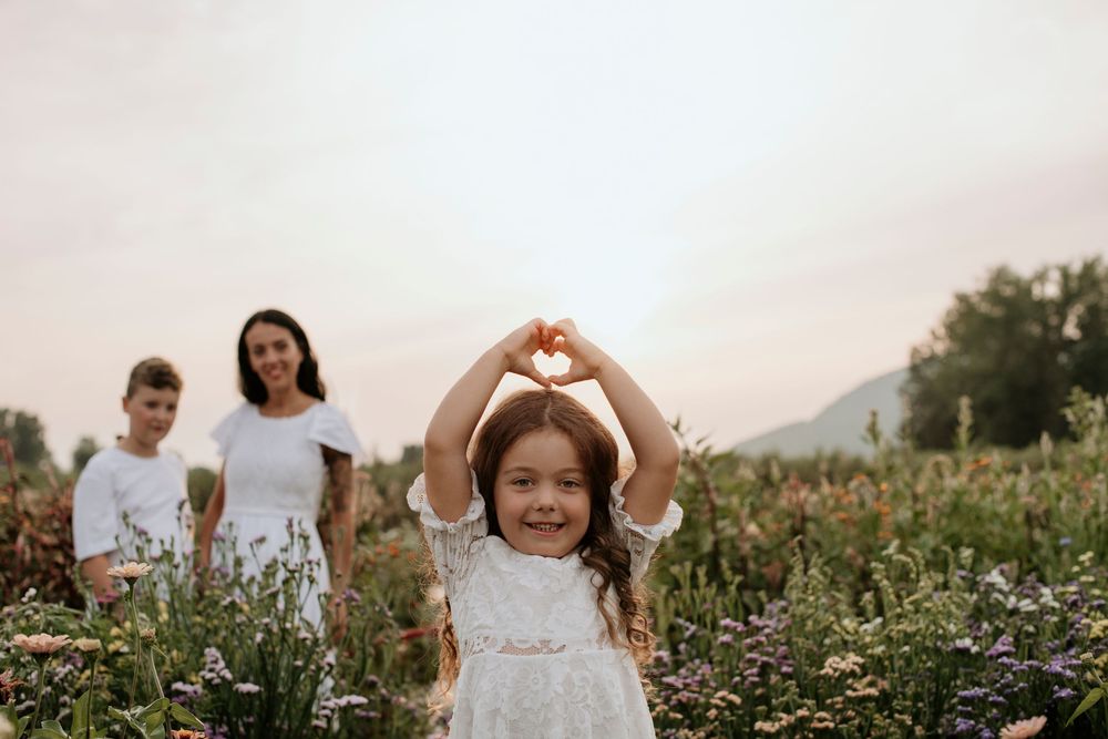 A couple forms a heart shape with their hands while standing in a wildflower meadow at sunset.