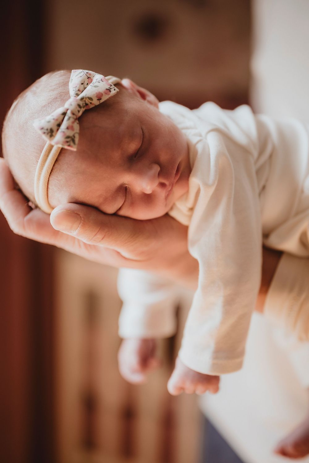 A sleeping newborn baby wearing a white onesie rests peacefully in a horizontal position.