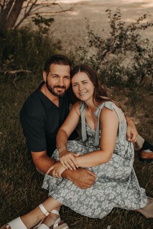 A couple sits together on grassy hillside at sunset sharing an intimate embrace in warm lightMichigan Engagement Photographer | Creative Art