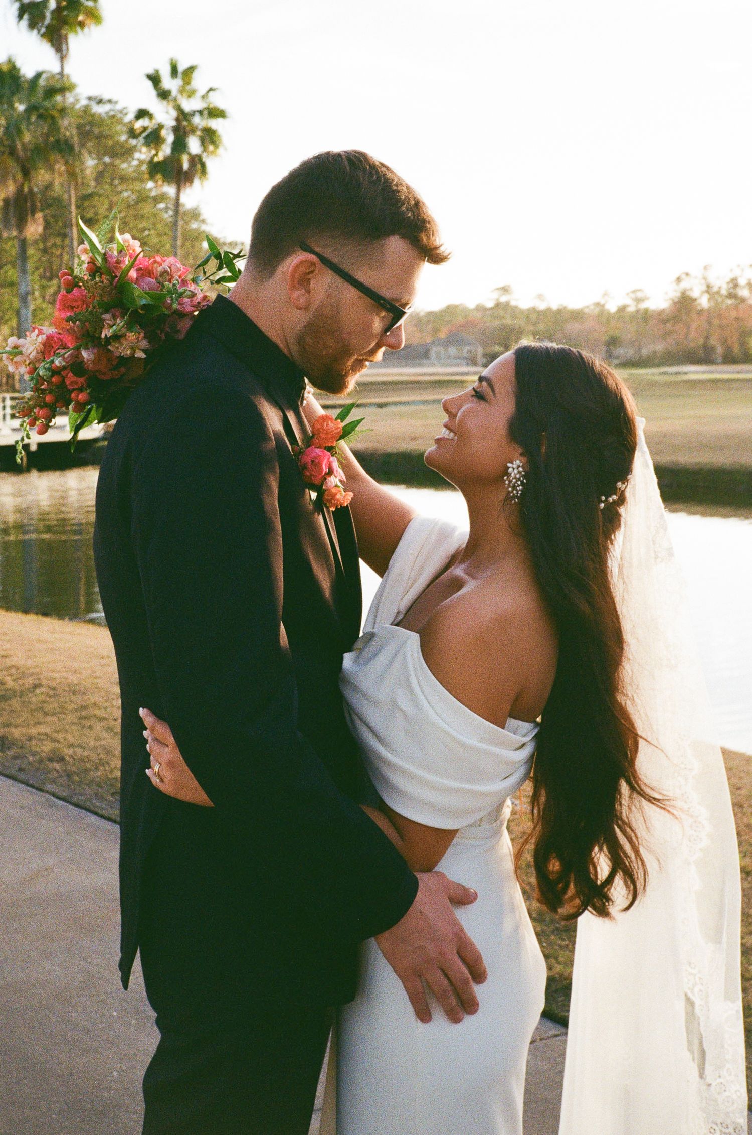 Bride and groom looking at each other lovingly while bride holds colorful bouquet.