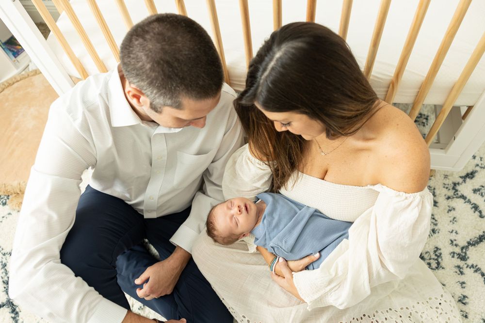 Parents gazing down at their newborn baby in a bright bedroom setting.