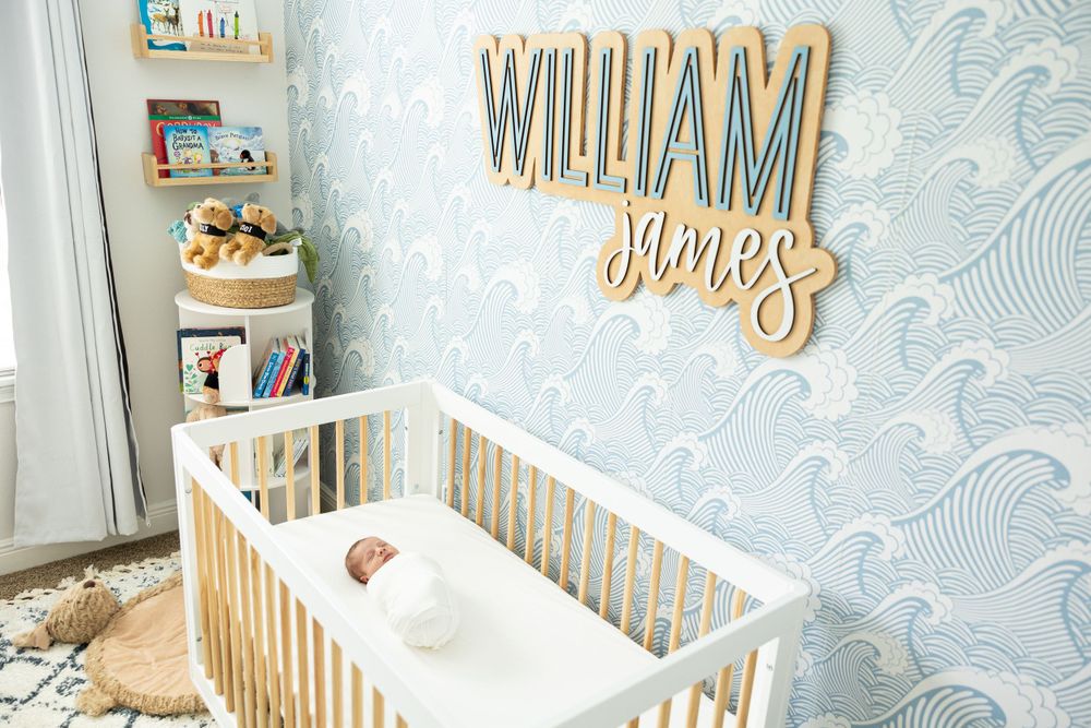 Modern nursery with blue wave wallpaper features white crib and wooden name sign.