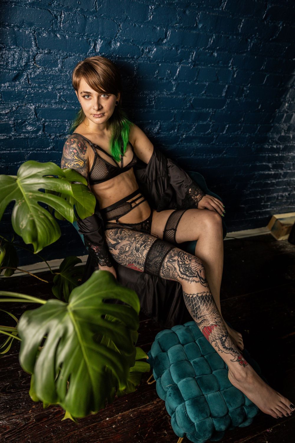 Model poses with monstera plants against blue brick wall.