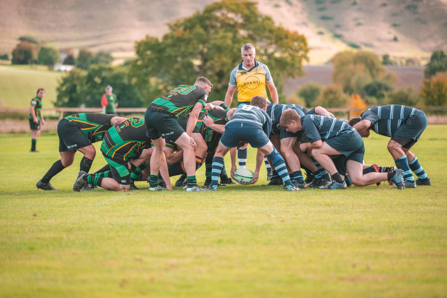 Rugby scrum formation with players locked together during a match on a grass field.