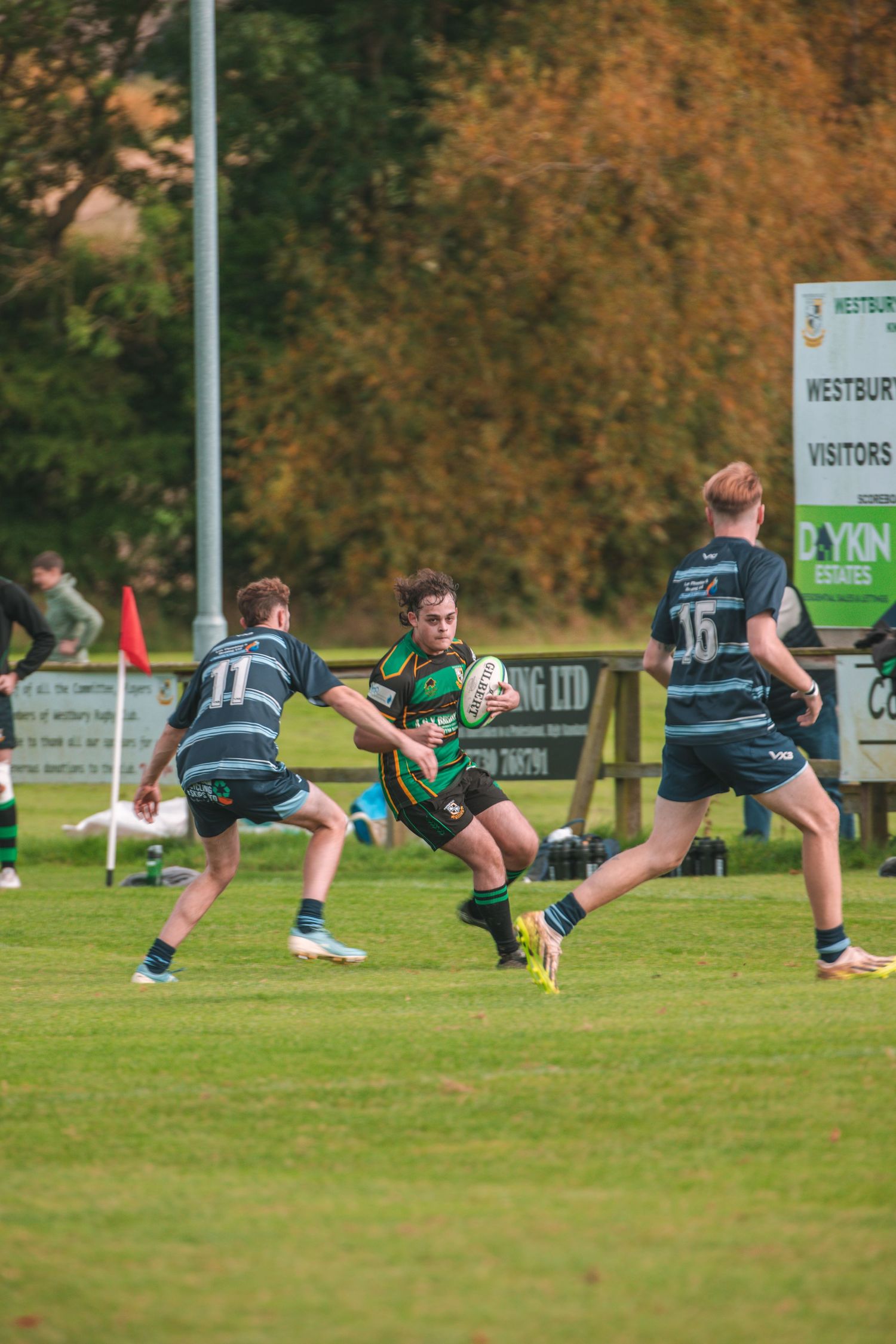 Rugby player carrying ball while evading defenders on grass field during match play.