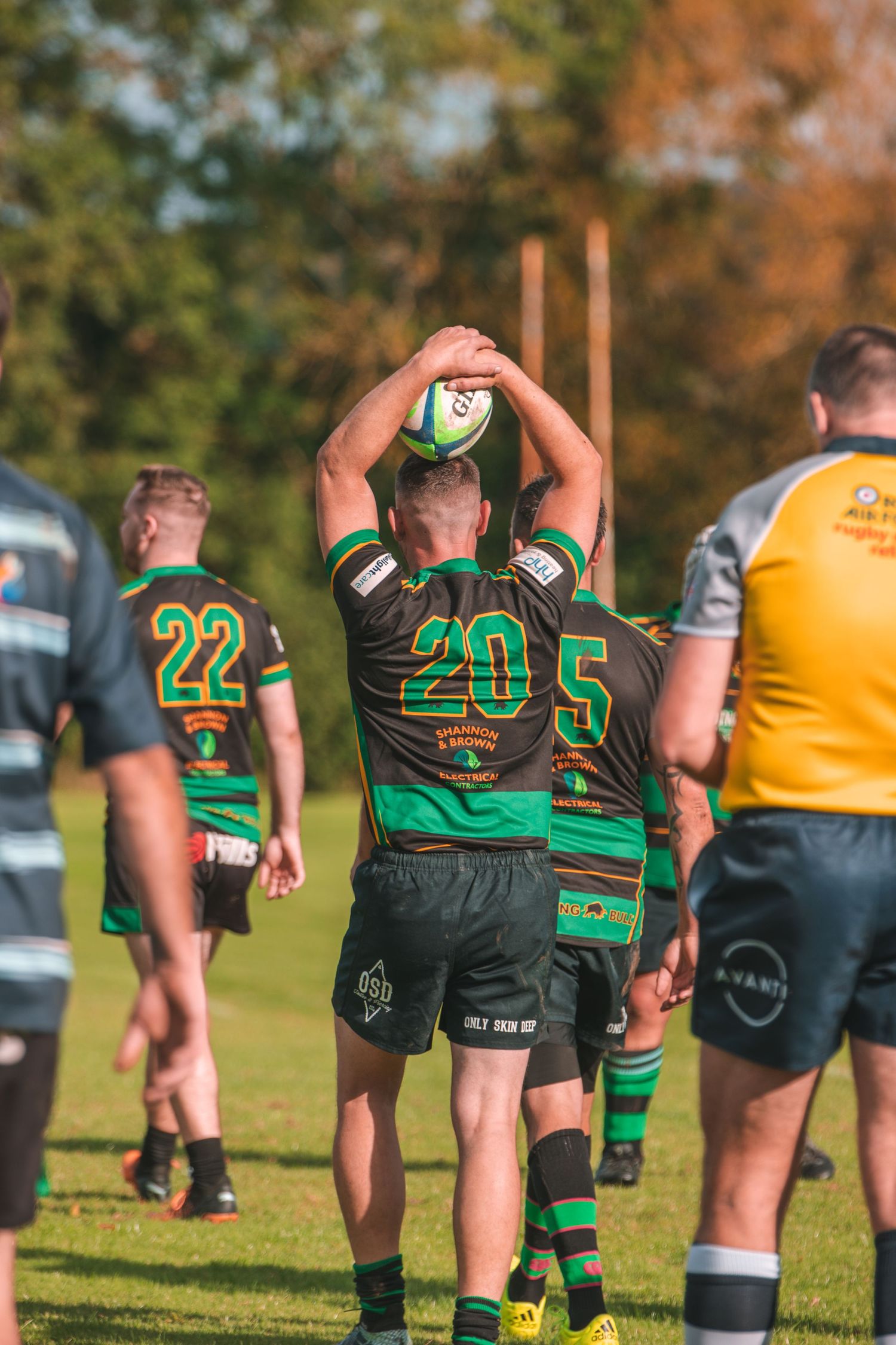 Rugby player in green jersey number 20 preparing for a line-out throw on sunny field.